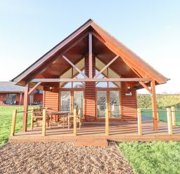 A wooden cabin with a patio and outdoor furniture surrounded by grass at Lodge 7 in South Hykeham