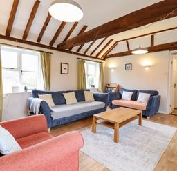 A living room with blue and red sofas a wooden coffee table and exposed wooden ceiling beams at The Brambles in Polstead