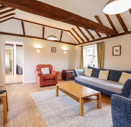 A living room with a blue sofa, red armchair, wooden coffee table, television, and exposed ceiling beams at The Brambles in Polstead
