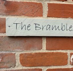 A sign reading The Brambles on a red brick wall at The Brambles in Polstead