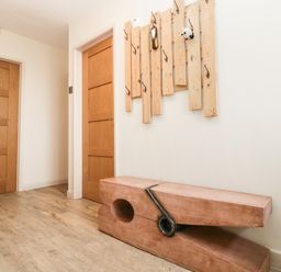 A hallway with wooden doors a wooden bench shaped like a clothespin and a wall-mounted wooden coat rack at Palace Bungalow in St Weonards