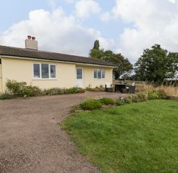 An exterior view of a bungalow with a gravel driveway a small garden and outdoor seating area at Palace Bungalow in St Weonards