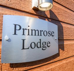 A metal sign with the words Primrose Lodge mounted on a wooden wall under a light at Primrose Lodge in Runswick Bay near Staithes