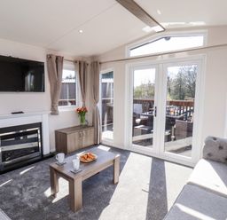 A living room with a wall-mounted TV fireplace sofa coffee table and glass doors leading to an outdoor seating area at Primrose Lodge in Runswick Bay near Staithes