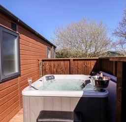 An outdoor hot tub next to a wooden building with a glass and a bottle in a metal ice bucket on the tub at Primrose Lodge in Runswick Bay near Staithes