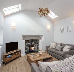A sitting room with two grey sofas a wooden coffee table a wood burning stove and a TV at Tan Y Coed - Nasareth Nasareth near Penygroes
