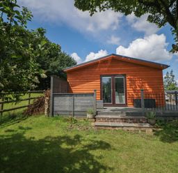 A wooden cabin with a small deck and glass doors surrounded by grass and trees at Harry's Lodge in Ashover