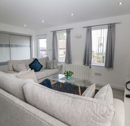 A living room with two grey sofas a glass coffee table a television and two windows with curtains at Harry's Lodge in Ashover