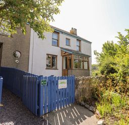 A white two-story house with wooden windows and blue gate surrounded by plants at Ynys Faelog Cottage Ynys Faelog near Menai Bridge