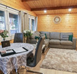 A living room with a grey sofa a round table with chairs flowers and windows at Buttermilk Bridge in Dungiven