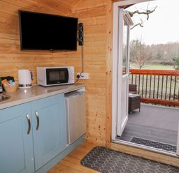 A kitchen corner with blue cabinets, microwave, kettle, a bottle, and a TV mounted on a wooden wall at Pine in Dungiven Londonderry