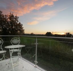A balcony with a metal table and two chairs overlooking a field at sunset at Upper Annex in Quemerford