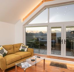 A small living room with a yellow sofa glass coffee table and large glass doors leading to a balcony at Upper Annex in Quemerford
