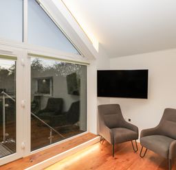 A room with two gray chairs a wall-mounted TV and large windows leading to a balcony at Upper Annex Quemerford