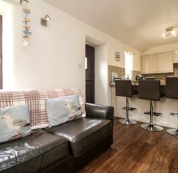 A kitchen area with three bar stools and a leather sofa with seagull cushions at The Old Piggeries in Gulval near Penzance