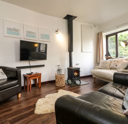 A living room with leather and fabric sofas a wood burning stove and television at The Old Piggeries in Gulval near Penzance