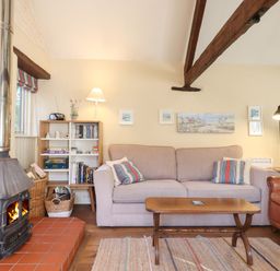 A living room with a wood stove fireplace a beige sofa a brown leather armchair wooden coffee table bookshelf and framed pictures on the wall at The Calf Pen in Colyton