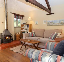 A living room with a wood burning stove sofa armchair coffee table and bookshelf at The Calf Pen in Colyton