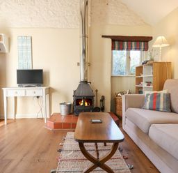 A living room with a sofa a wood stove a coffee table and a TV on a table at The Calf Pen in Colyton