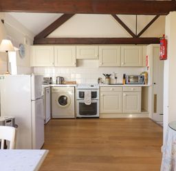 A kitchen with white cabinets appliances and wooden floor at The Bull Pen in Colyton