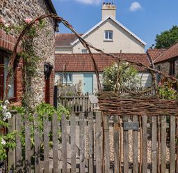 A garden area with a wooden gate and vine decorations outside stone cottages at The Hay Loft in Colyton