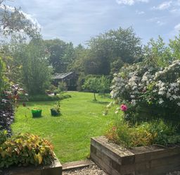 A garden with green grass trees and a greenhouse in the background at The Hay Loft in Colyton