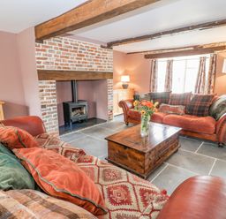 A living room with two sofas a wooden coffee table a brick fireplace with a wood stove and exposed ceiling beams at The Old Bakehouse in Avebury