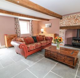 A living room with a red sofa wooden coffee table with flowers wood burning stove and exposed wooden ceiling beams at The Old Bakehouse in Avebury