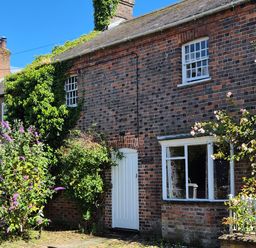 A brick house with a white door and windows and plants growing around it at The Old Bakehouse in Avebury