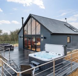 A modern house with a large glass front and dark wood deck with hot tub and outdoor seating at Stags Mount in Thornton Dale