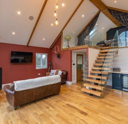 A living room with brown leather sofas a wood stove and a staircase leading to a loft at Stags Mount in Thornton Dale