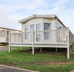 A mobile home with a porch and railing on grass next to a paved path at Forest Star in Cayton