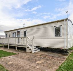 A beige mobile home with a small porch and steps on a paved area with grass around at Forest Star in Cayton
