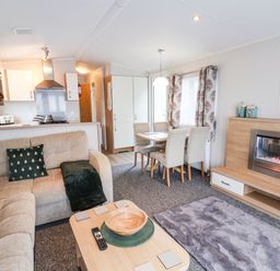 A living room with a beige sofa and green cushions a wooden coffee table dining table with four chairs and an electric fireplace at Forest Star in Cayton