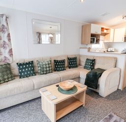 A living room with a beige sofa with green pillows a wooden coffee table and a kitchen in the background at Forest Star in Cayton