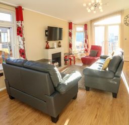 A living room with two sofas a red chair a wall-mounted TV and large windows at Dream Catcher Lodge in Carnforth