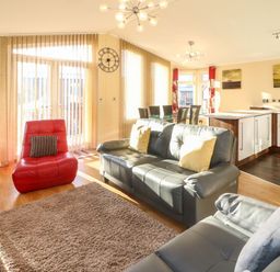 An open living area with gray sofas, a red chair, dining table with chairs, kitchen island, and tall windows at Dream Catcher Lodge in Carnforth