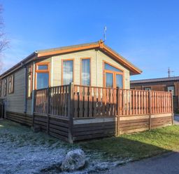 A wooden cabin with a fenced porch on a grassy area at Dream Catcher Lodge in Carnforth