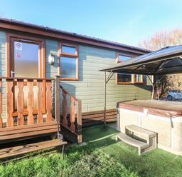 An outdoor area with a wooden bench a hot tub with a cover and steps and a wooden side door with windows at Dream Catcher Lodge in Carnforth