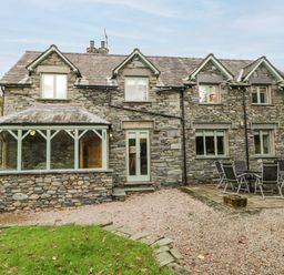A stone house with green framed windows and doors and an outdoor patio with a table and chairs at Scandale Bridge Cottage in Ambleside