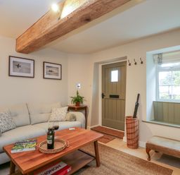 A living room with a beige sofa coffee table and wooden door at Thorn Cottage in Fairford