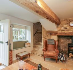 An entrance area with a white door stone steps a leather armchair fireplace and window seat at Thorn Cottage in Fairford