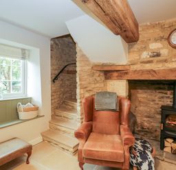 A sitting area with a leather armchair near a wood burning stove and stone stairs at Thorn Cottage in Fairford