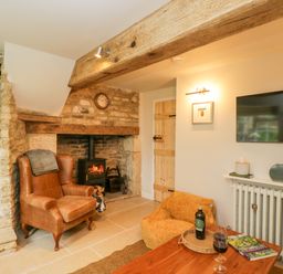 A living room with a leather armchair a fireplace with a wood burning stove a wooden door and a mounted TV at Thorn Cottage in Fairford