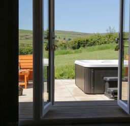 An open door leading to a patio with a hot tub and wooden bench outside at Oak in Ulverston