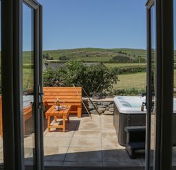A patio with a wooden bench and table set and a hot tub with steps in a countryside setting at Rowan in Ulverston