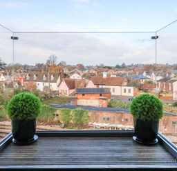 View of rooftops and houses from a balcony with glass railing and two potted plants at Woodbridge Penthouse in Woodbridge