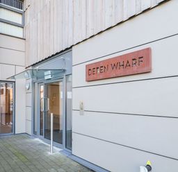 Entrance to a building with glass double doors and a sign reading deten wharf on the wall at Woodbridge Penthouse in Woodbridge