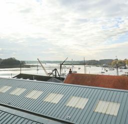 A view of a harbor with boats and cranes behind metal and tiled rooftops at Woodbridge Penthouse in Woodbridge