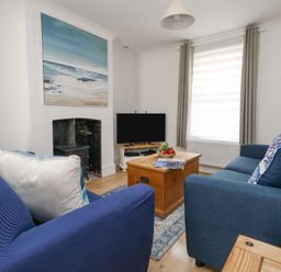 A living room with two blue sofas a wooden chest coffee table a television and a painting of the sea at Day Cottage in Weymouth